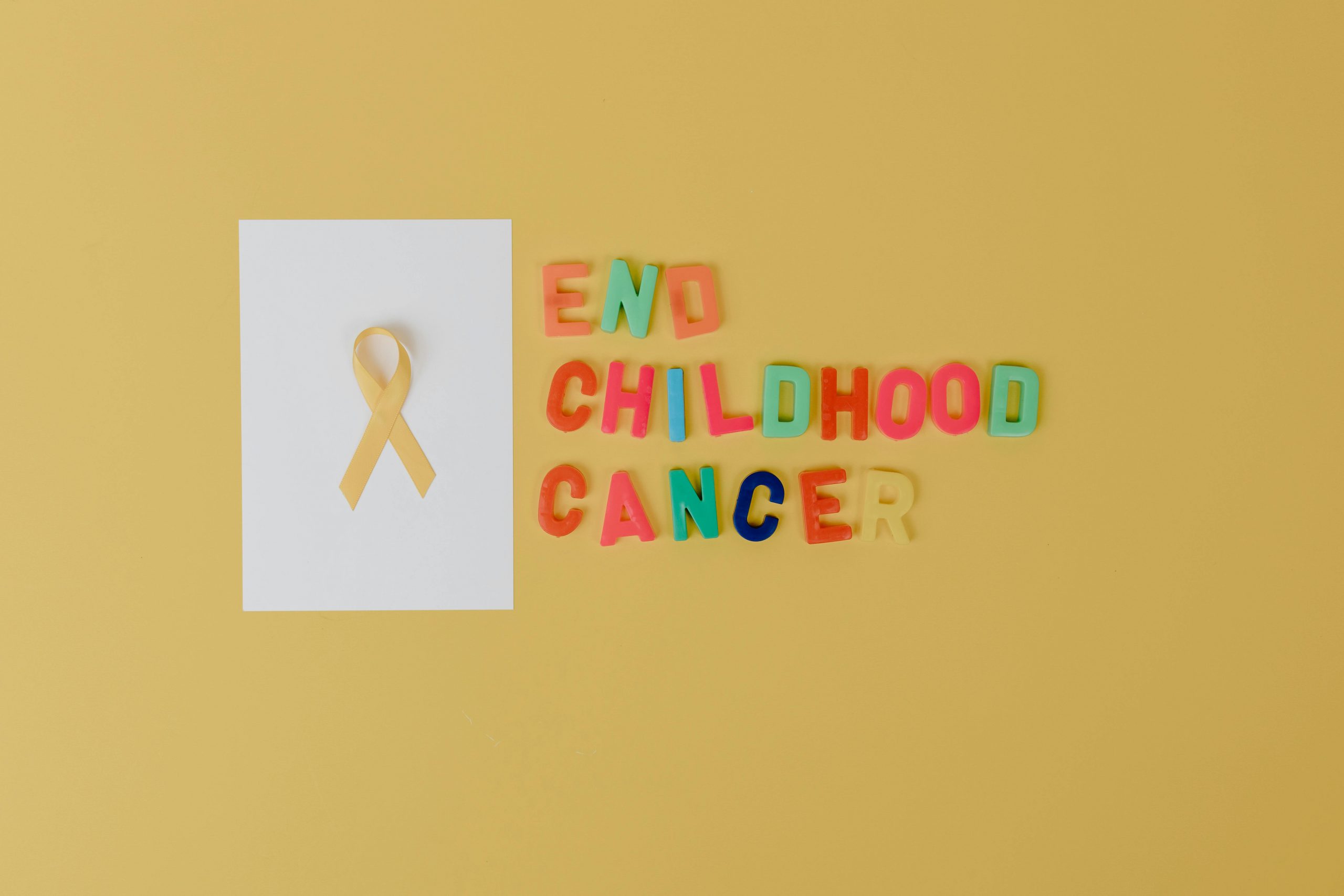 pexels photo 8385220 8385220 Yellow ribbon and colorful letters for childhood cancer awareness on a yellow background.